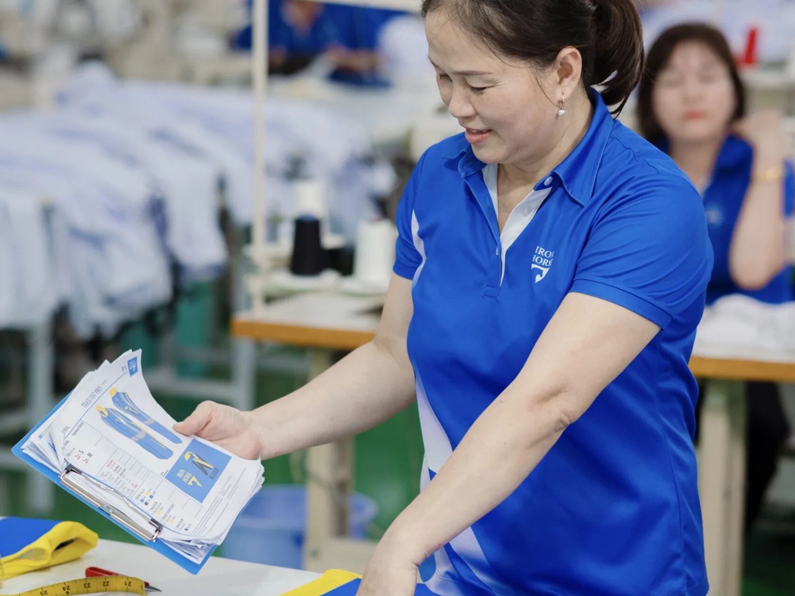 Iron Horse team member checking a small sportswear order against its specification sheet before packing, on the factory floor in Ho Chi Minh City